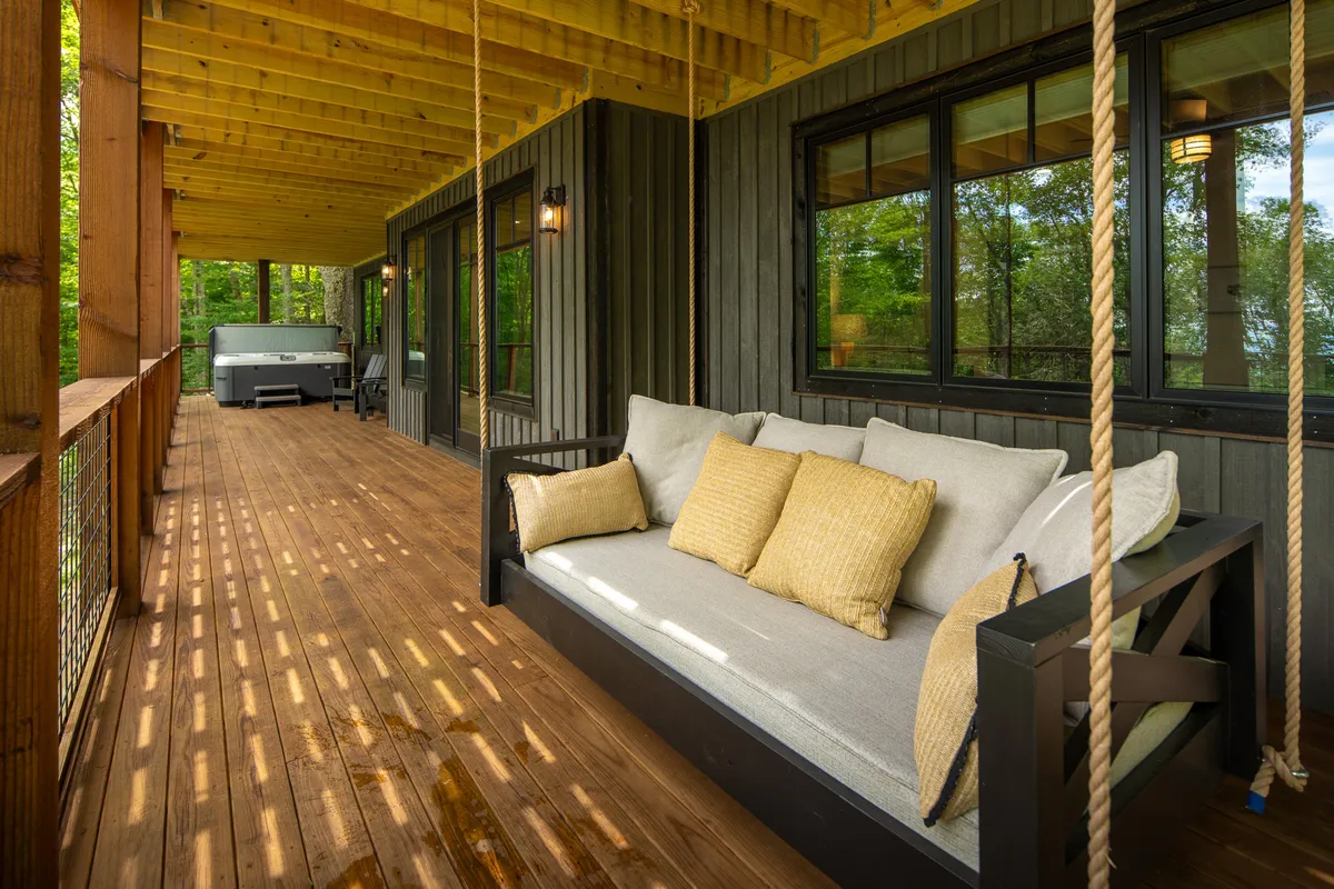 This exterior shot focuses on a lower deck area that includes a comfortable swing sofa and a well-placed hot tub, all surrounded by lush greenery. The scene radiates tranquility and sociability, perfect for unwinding outdoors and enjoying nature in comfort.