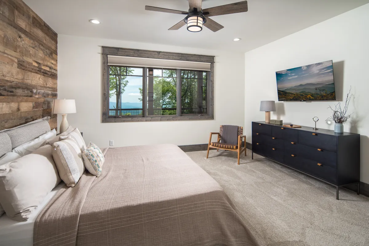 A serene bedroom with a plush bed, large windows letting in natural light, a dresser, TV, and a cozy accent chair. The room balances relaxation and modern amenities, providing both comfort and entertainment for unwinding after a day of adventure.