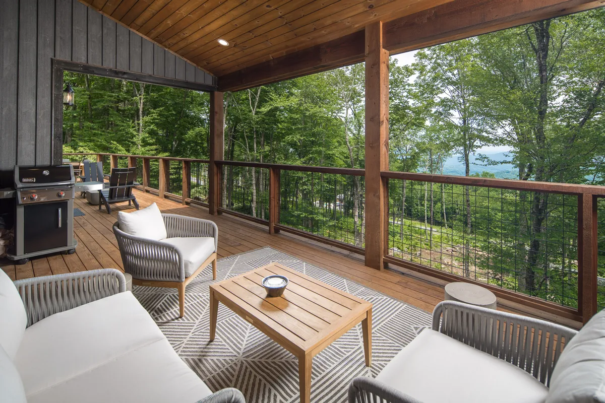 A wooden deck furnished with comfortable seating overlooks a tranquil view of trees, providing a peaceful extension of the indoor gathering spaces. The setting hints at both relaxation and the opportunity to host social gatherings outdoors.