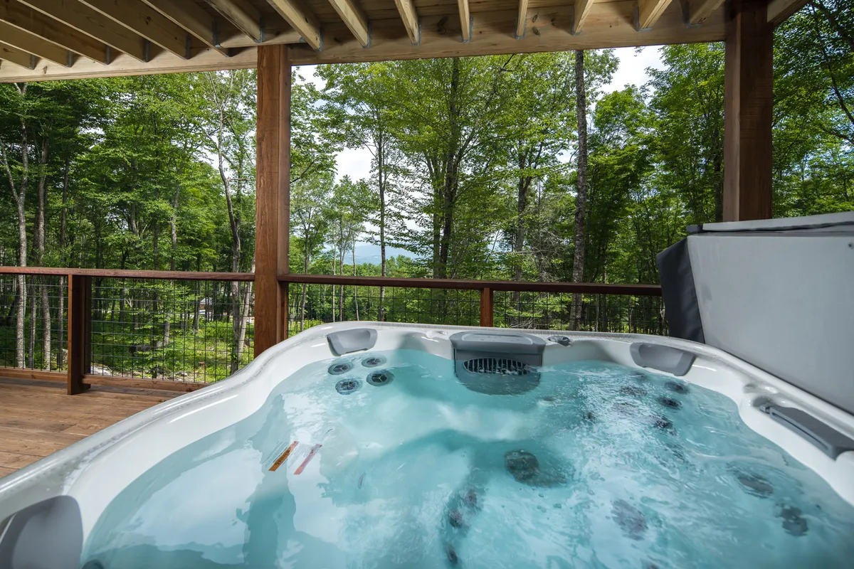 A serene exterior view of a hot tub on a wooden deck, embraced by greenery. The inviting water and tranquil natural setting suggest relaxation after a day of outdoor activities, with ample space for friends and family to unwind together.