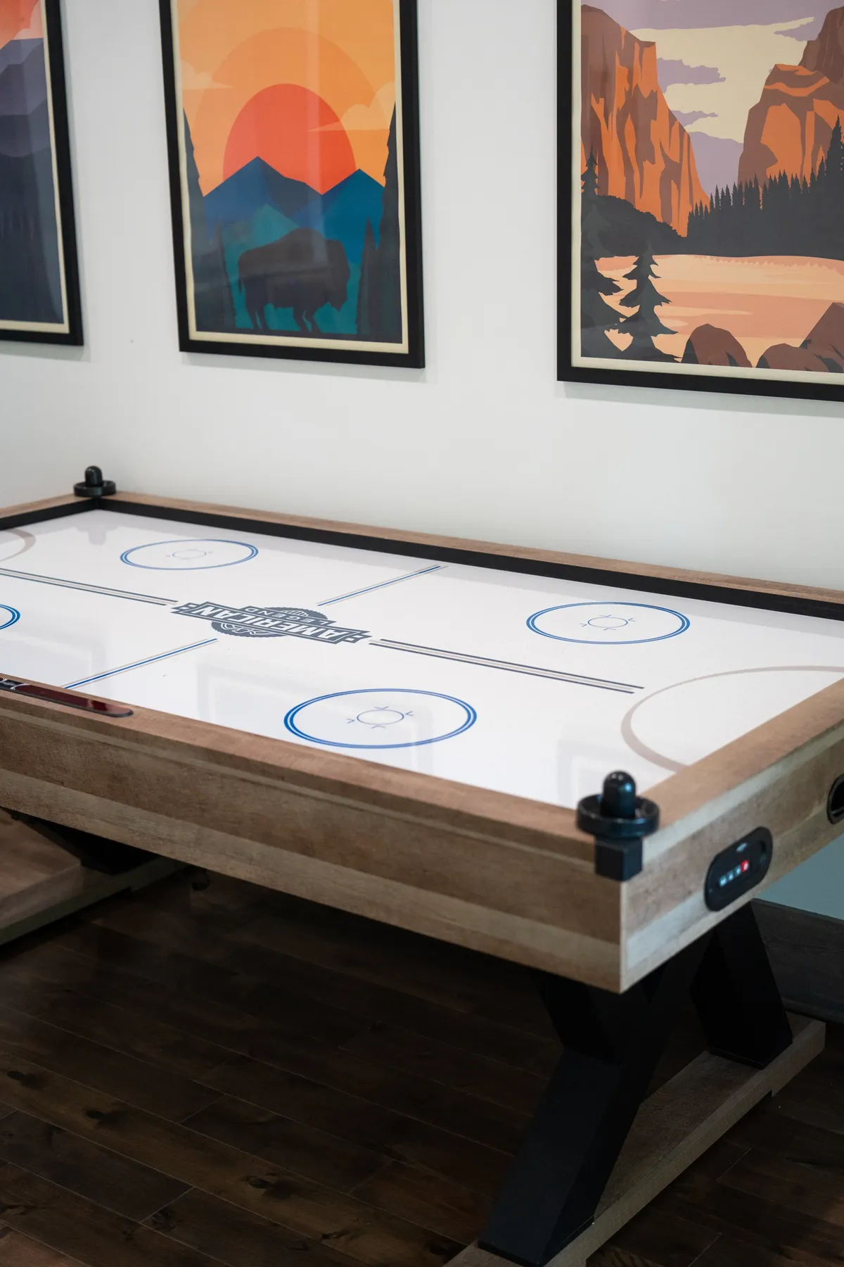 The image depicts an interior game room featuring an air hockey table as the main focal point. The room is decorated with framed artwork on the walls, creating an inviting and lively atmosphere ideal for family fun and friendly competition.