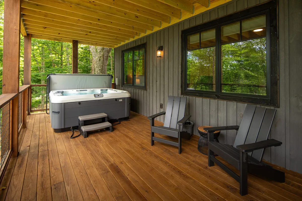 A tranquil deck with an inviting hot tub and Adirondack chairs, set against a backdrop of trees. The space is designed for relaxation, stargazing, and enjoying quiet moments in the fresh mountain air.