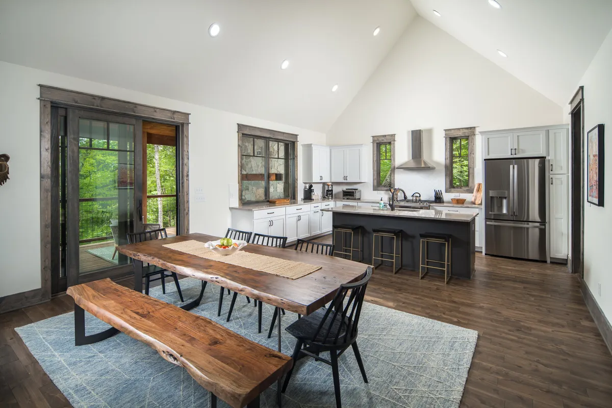 A rustic live-edge dining table is positioned near expansive windows, with the kitchen island and generous cabinetry visible in the background. The arrangement is bathed in natural light, creating an inviting atmosphere ideal for family meals and festive occasions.
