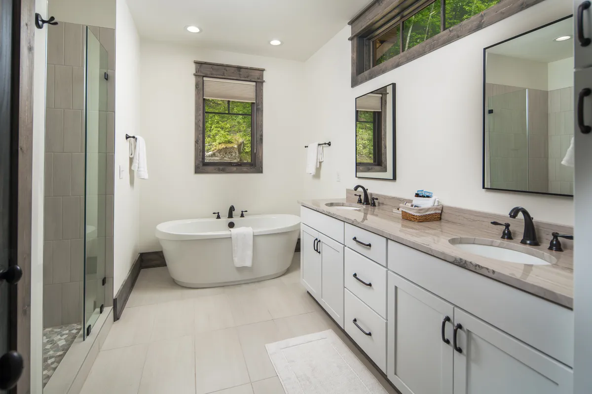 A bright, elegant bathroom with a freestanding tub, double vanity, and large windows, offering a serene setting for relaxation and self-care. The clean lines and modern fixtures evoke a sense of spa-like luxury and privacy.