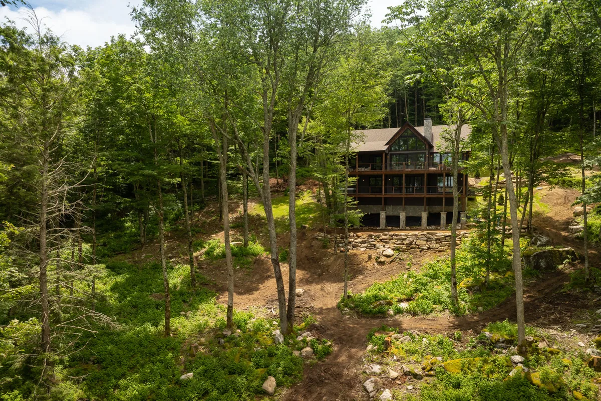 The home's exterior is nestled among towering trees, with a landscaped lawn perfect for outdoor gatherings. The tranquil setting highlights the privacy of the two-acre lot and the opportunity for wildlife viewing, morning coffee, or evening campfires in nature.