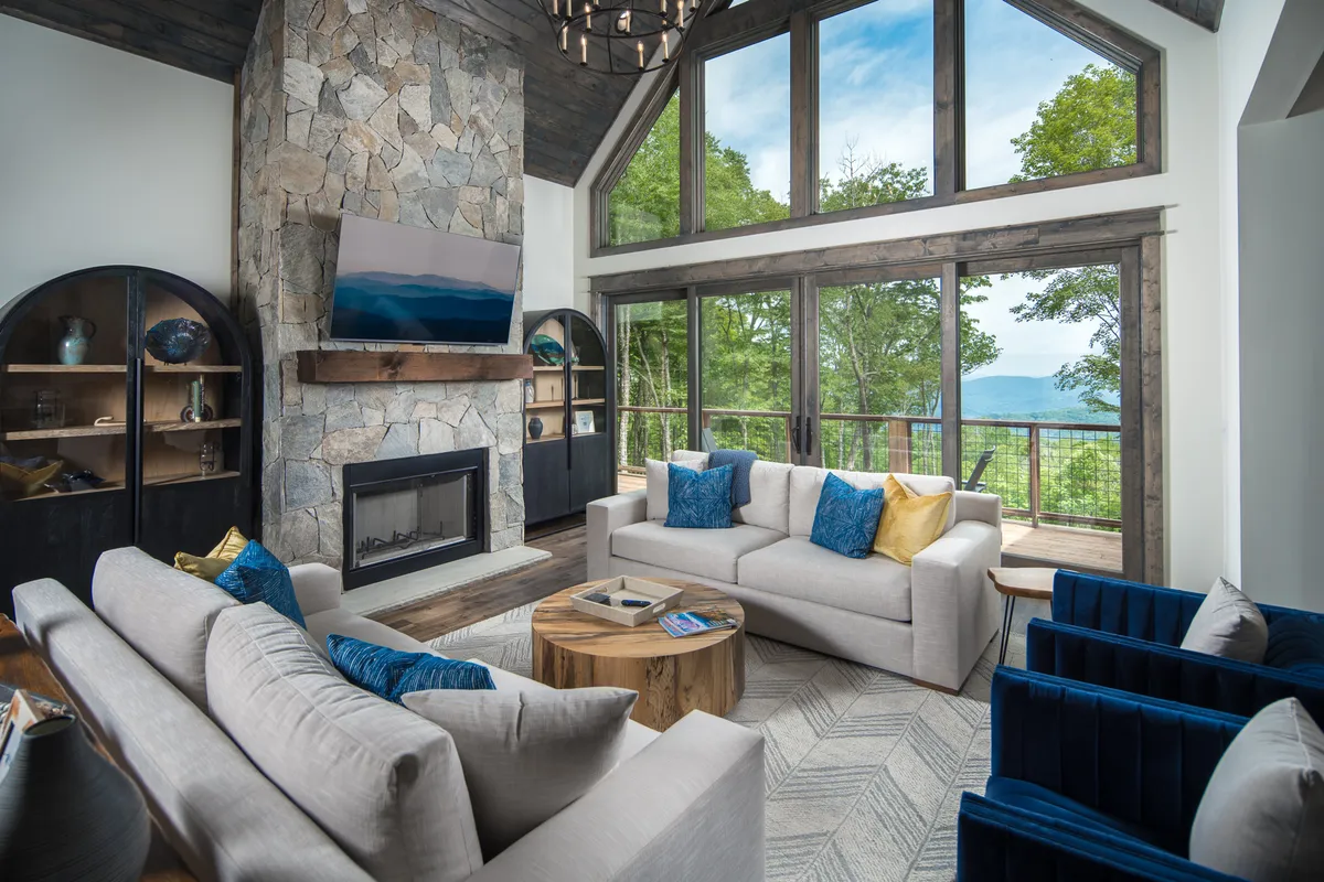 A cozy living room with a large stone fireplace, expansive windows framing mountain views, and comfortable seating arranged for relaxation or family gatherings. The natural light and decor create a warm, inviting atmosphere ideal for unwinding after outdoor adventures.